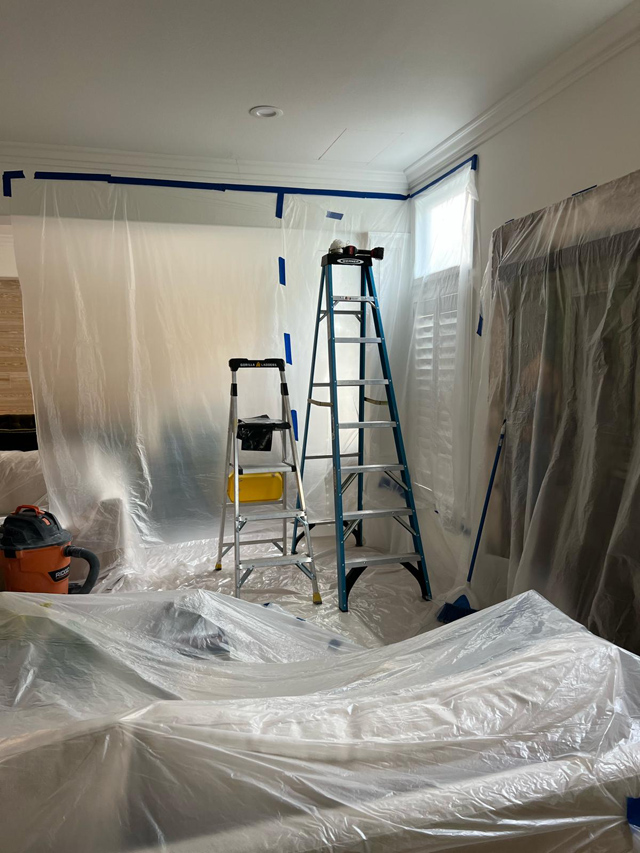 Room being painted; furniture covered in protective plastic.